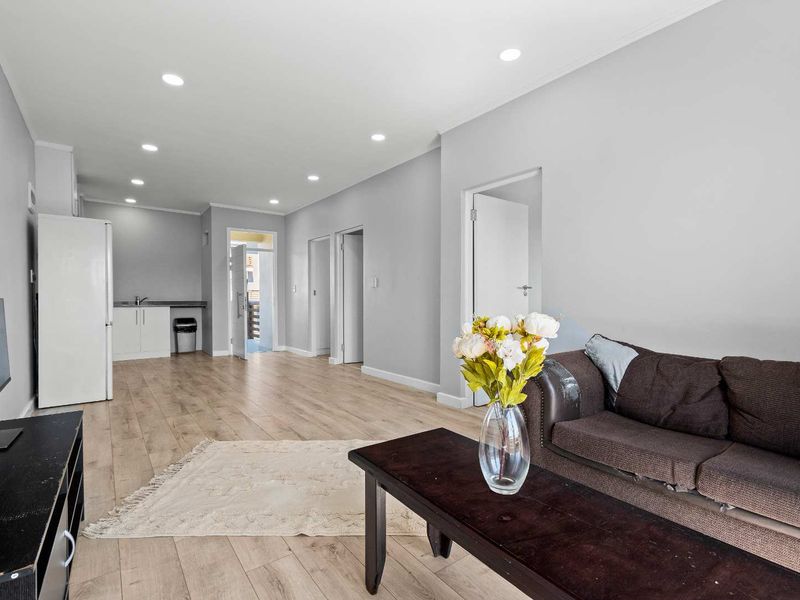 An open-plan living area featuring light-toned laminate flooring, recessed downlights, and a compact kitchenette with built-in cabinetry.