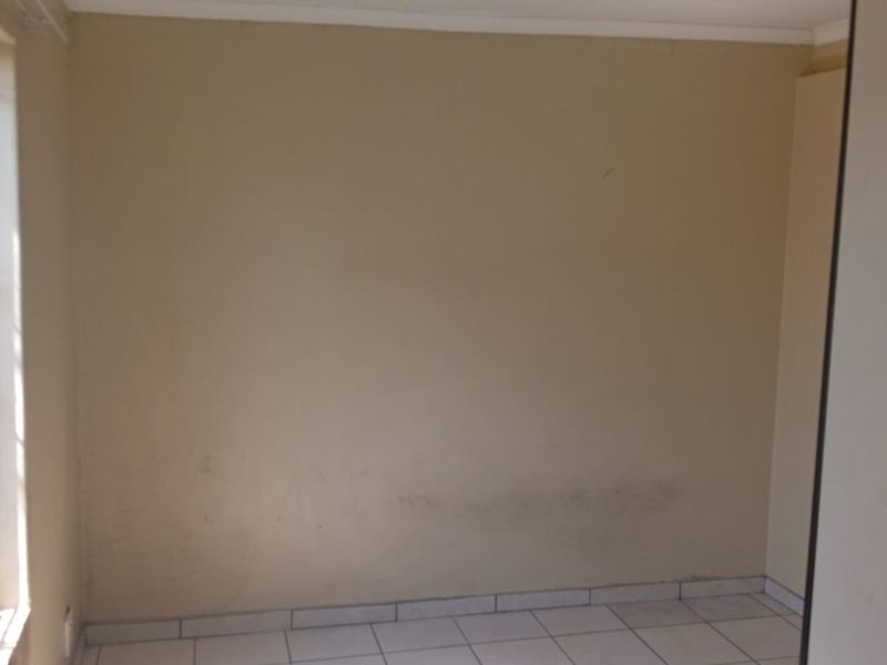 An empty bedroom featuring tiled flooring and a window with a security gate, requiring minor cosmetic updates to the wall finishes.
