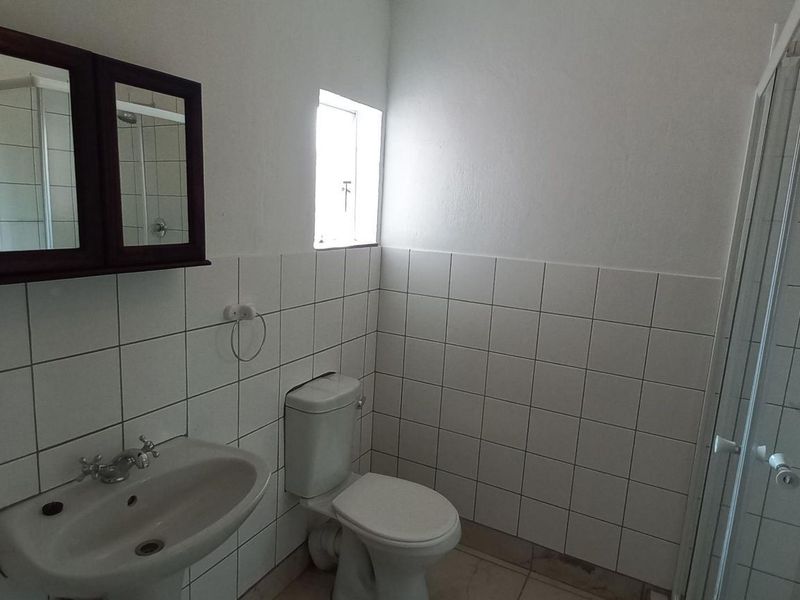 A functional bathroom featuring a pedestal basin, toilet, and a glass-enclosed shower with tiled walls and a wall-mounted medicine cabinet.