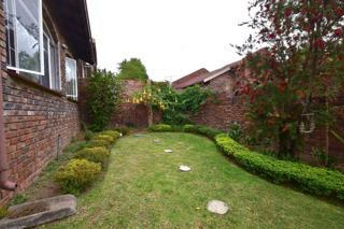 A private rear garden area featuring a manicured lawn, established hedging, and face brick boundary walls, accessible from the main dwelling.
