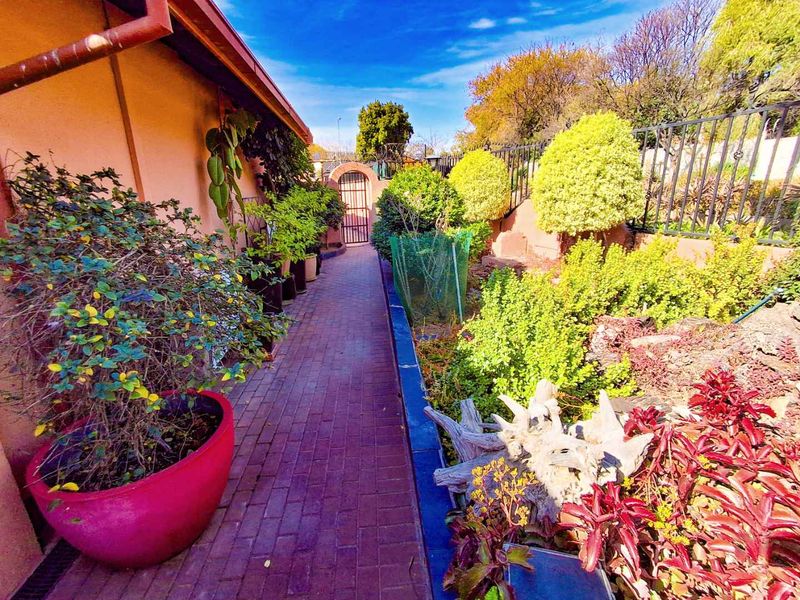 A well-maintained side garden featuring a brick-paved walkway, established landscaping, and secure metal perimeter fencing leading to a rear gate.