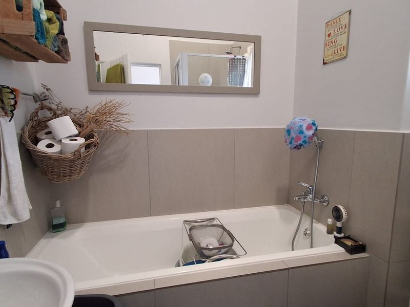 A functional bathroom featuring a bathtub with a handheld shower mixer, neutral wall tiling, and a wall-mounted mirror.