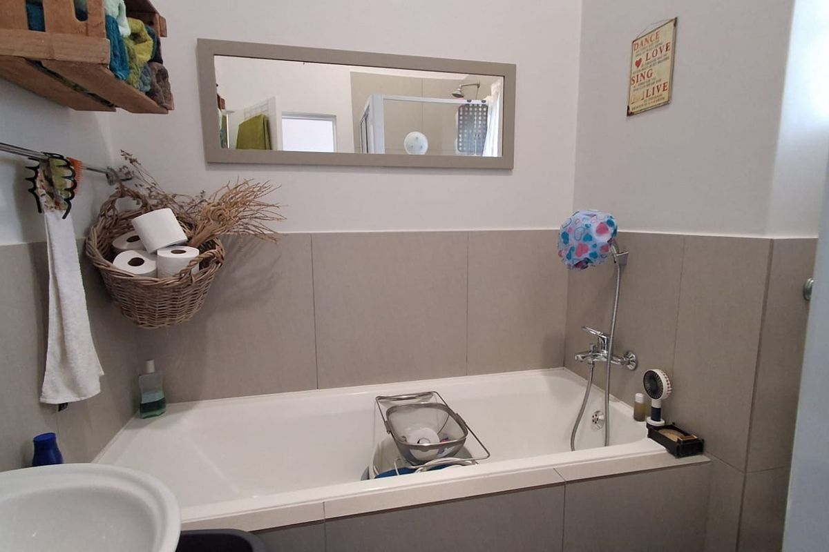 A functional bathroom featuring a bathtub with a handheld shower mixer, neutral wall tiling, and a wall-mounted mirror.