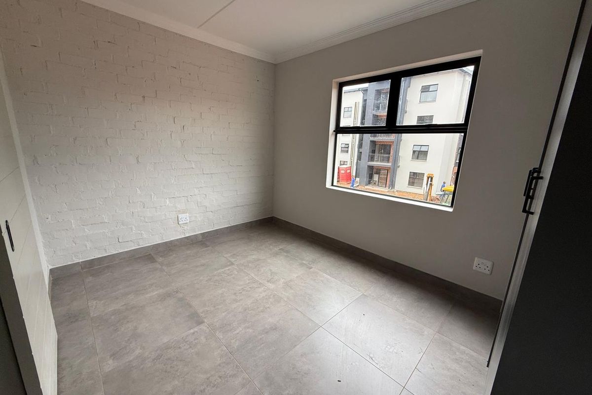 A bright, empty bedroom featuring neutral grey floor tiles, a painted brick accent wall, and a modern black-framed window.