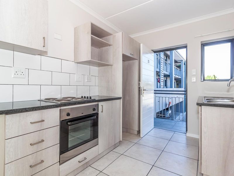 Modern kitchen featuring light wood-grain cabinetry, dark laminate countertops, built-in oven and hob, subway tile backsplash, and direct access to an exterior balcony.