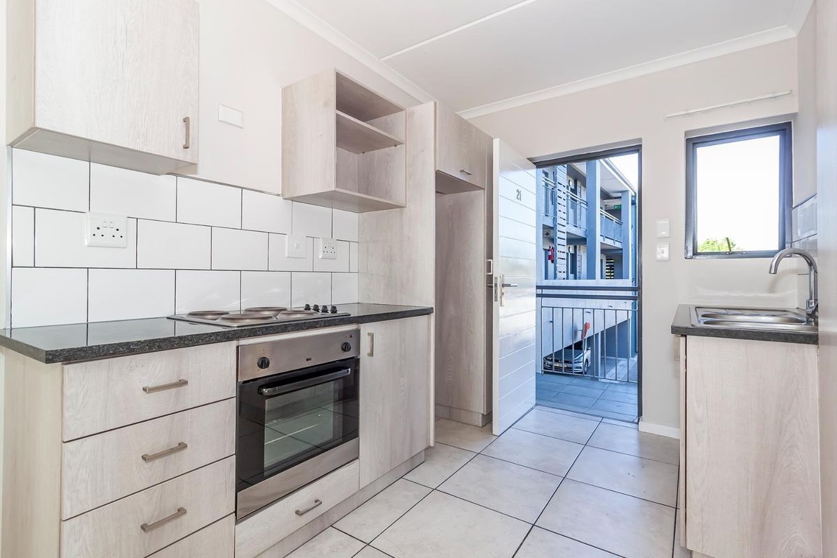 Modern kitchen featuring light wood-grain cabinetry, dark laminate countertops, built-in oven and hob, subway tile backsplash, and direct access to an exterior balcony.