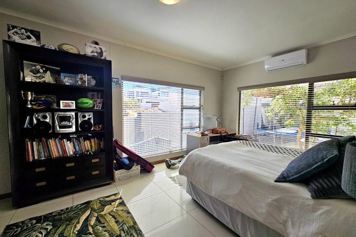 A well-lit bedroom featuring tiled flooring, large windows with horizontal blinds, and a wall-mounted air conditioning unit.