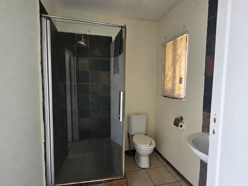 A functional bathroom featuring a glass-enclosed shower, toilet, and wall-mounted basin with tiled finishes throughout.