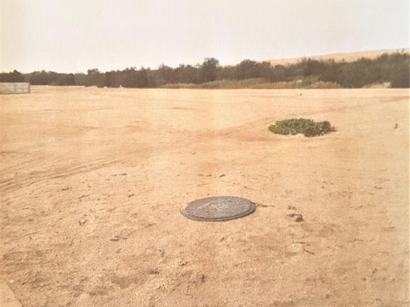 A view of a vacant residential plot featuring level ground and a visible manhole cover.
