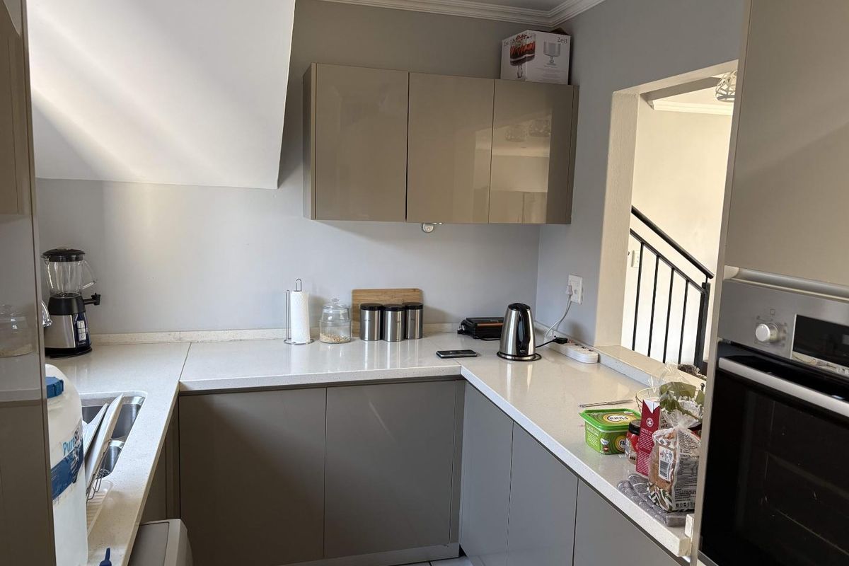 A modern kitchen featuring sleek taupe cabinetry, stone countertops, and a built-in oven, with a convenient pass-through window overlooking the staircase.