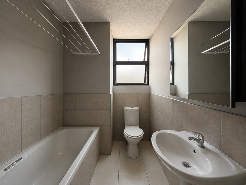 A clean, functional bathroom featuring a bathtub, pedestal basin, toilet, and neutral wall tiling with a large mirror.
