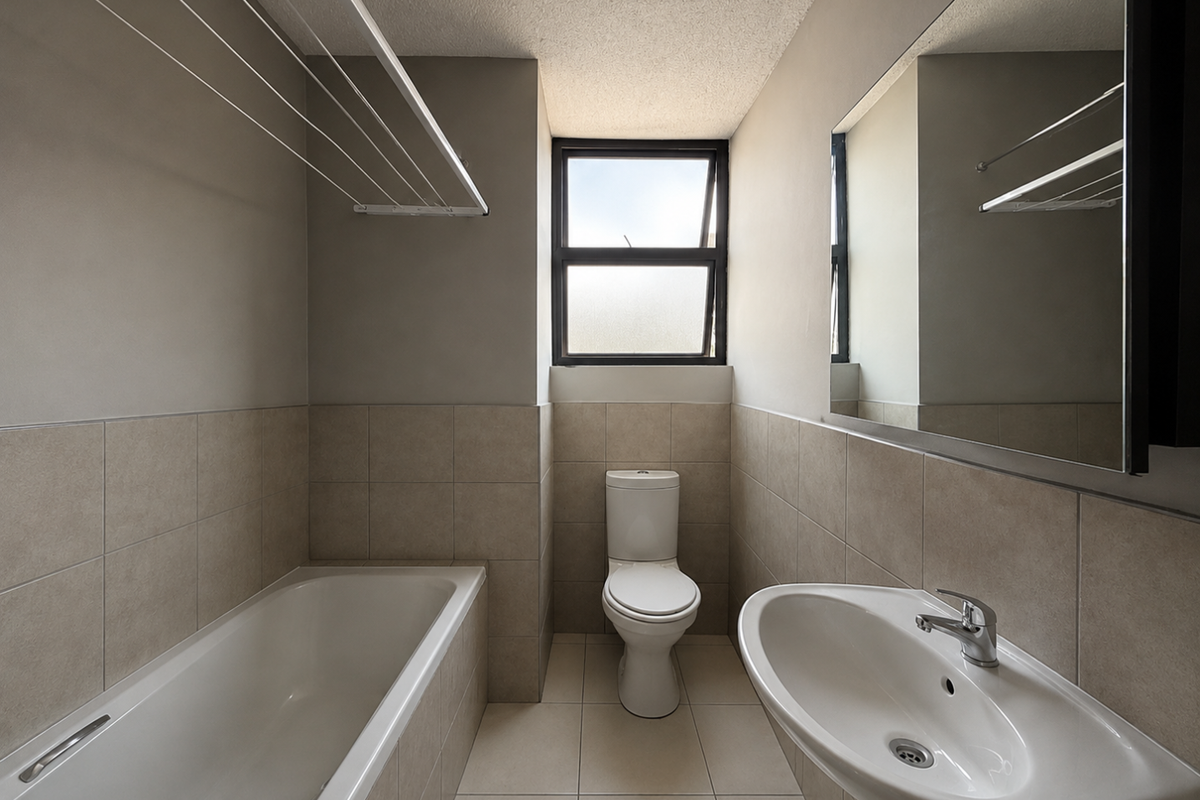 A clean, functional bathroom featuring a bathtub, pedestal basin, toilet, and neutral wall tiling with a large mirror.