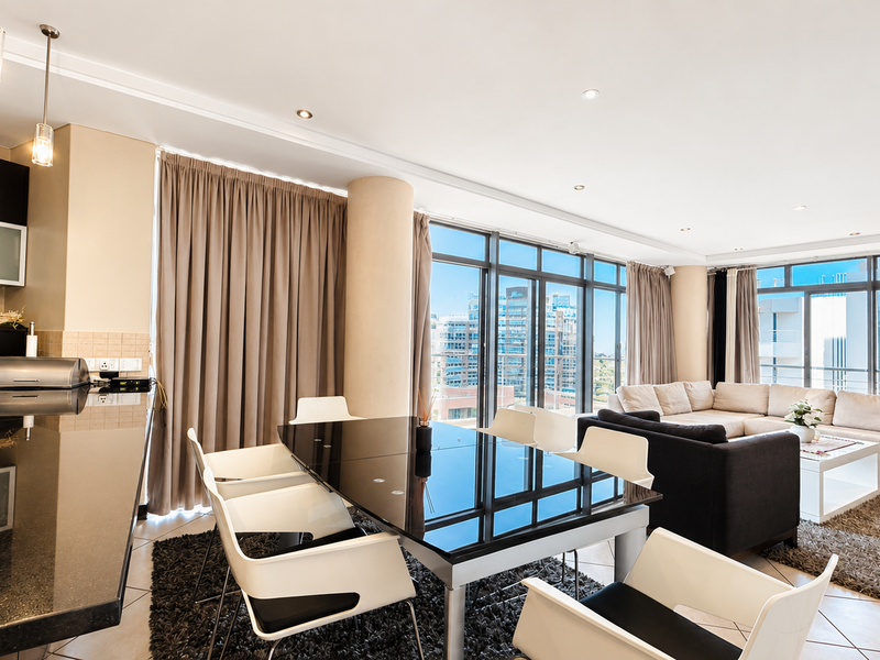 Spacious open-plan living and dining area featuring modern kitchen cabinetry, granite countertops, and expansive floor-to-ceiling windows with city views.