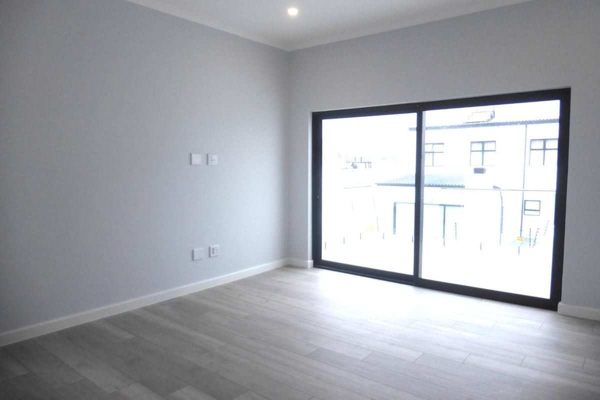 A bright, empty bedroom featuring modern laminate flooring, neutral walls, and a large sliding glass door providing natural light.