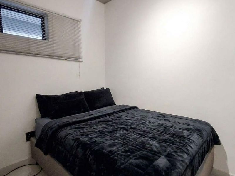 A simple bedroom featuring a horizontal window with a fitted blind and neutral wall finishes.