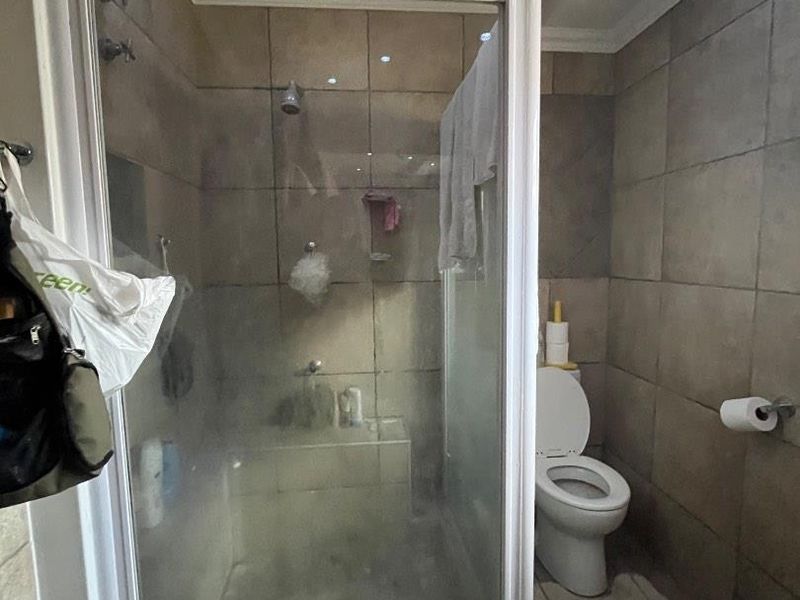 A functional bathroom featuring a glass-enclosed shower, toilet, and neutral wall and floor tiling with recessed lighting.