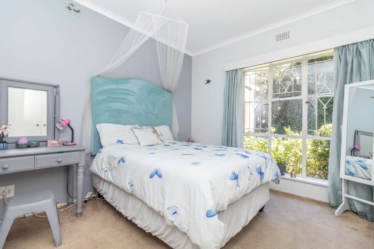 A well-lit bedroom featuring large windows that provide natural light and views of the garden, finished with neutral wall tones and carpeted flooring.