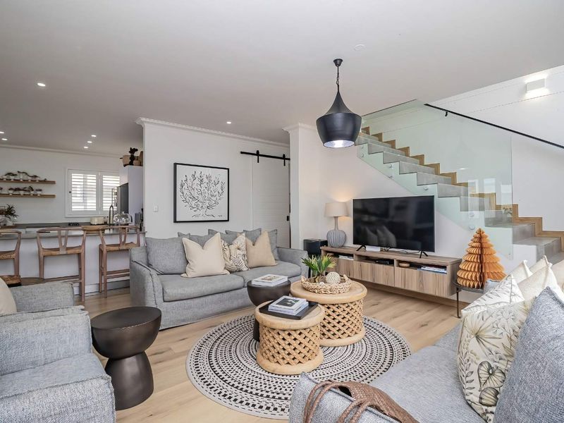 Modern open-plan living area featuring timber flooring, a contemporary glass balustrade staircase, and a seamless transition to a well-appointed kitchen.