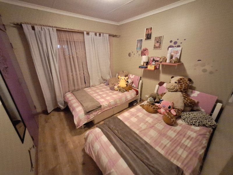 A bedroom featuring laminate flooring and cove cornice detailing, currently configured with two beds.