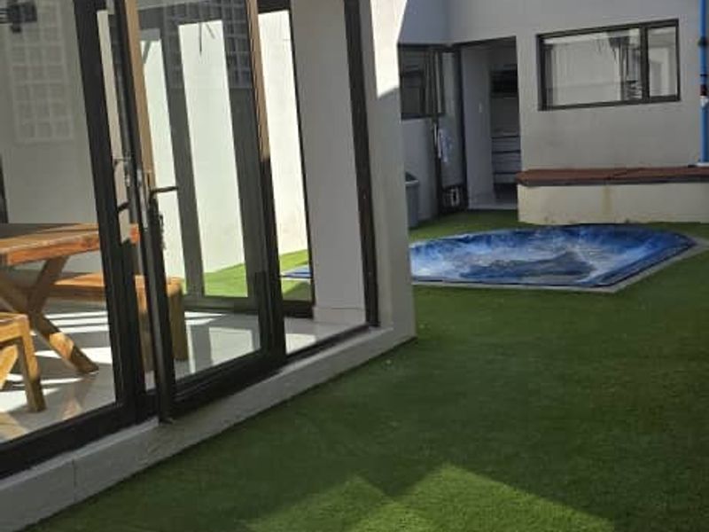 Rear courtyard area featuring artificial lawn, a built-in spa, and direct access to the interior living space through sliding glass doors.