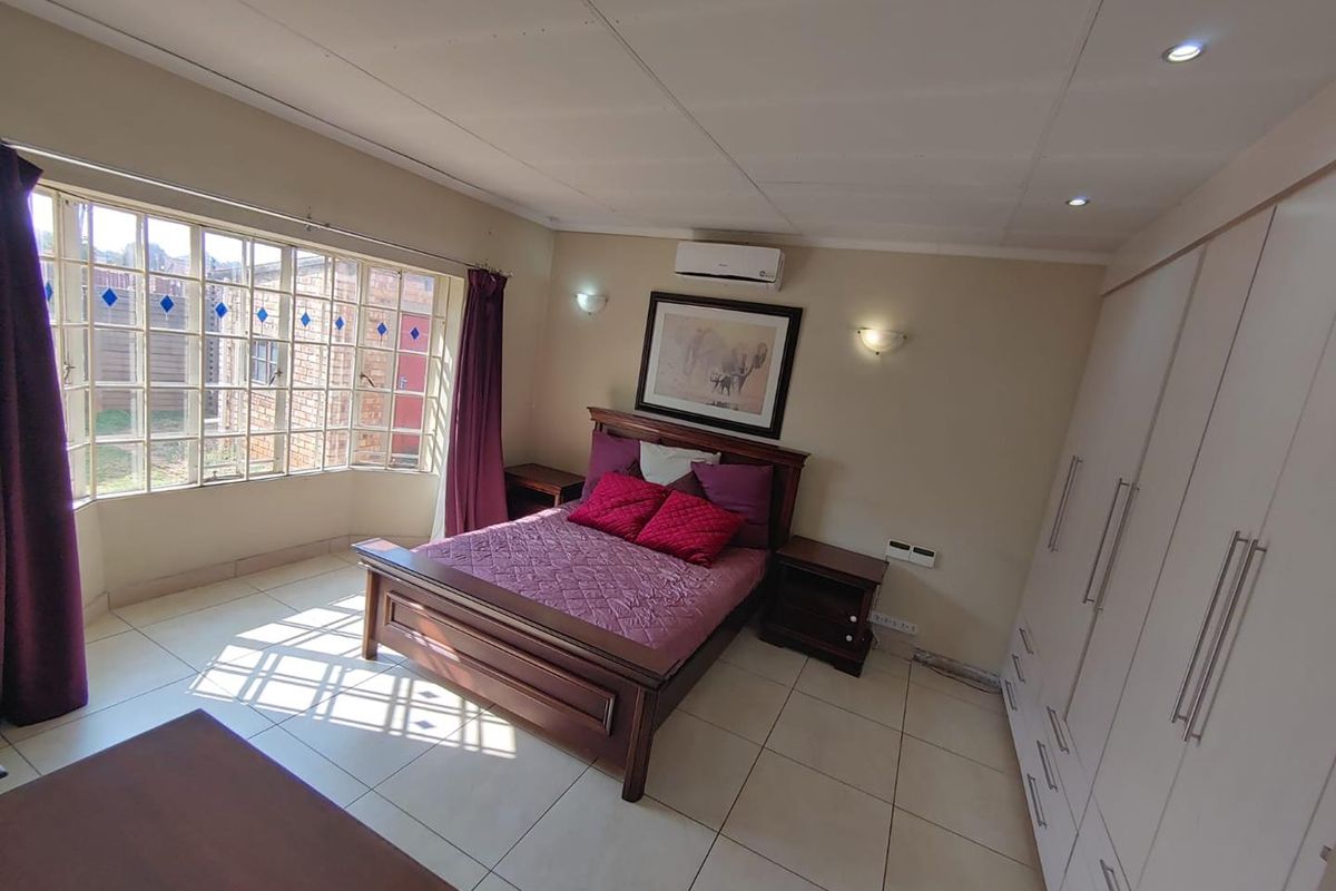 Spacious bedroom featuring large bay windows, built-in cupboards, tiled flooring, and an integrated air conditioning unit.