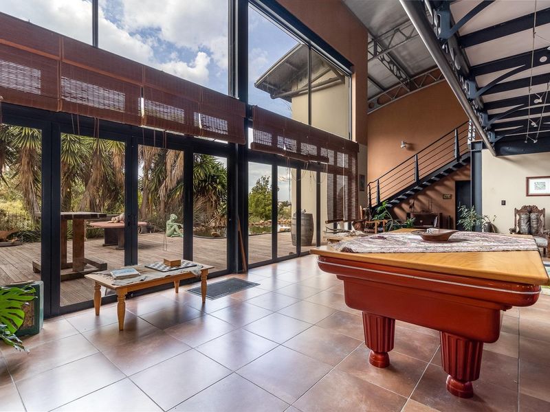Spacious double-volume living area featuring floor-to-ceiling windows, exposed steel roof trusses, and direct access to an outdoor deck.