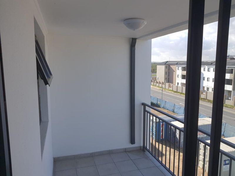A clean, covered balcony featuring tiled flooring, a metal safety balustrade, and a view of the surrounding residential area.