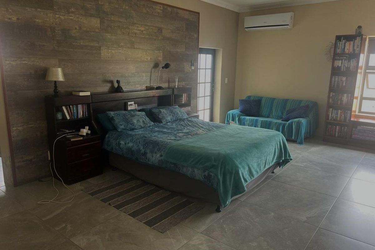 Spacious bedroom featuring large format floor tiles, a wood-look feature wall, and a wall-mounted air conditioning unit.