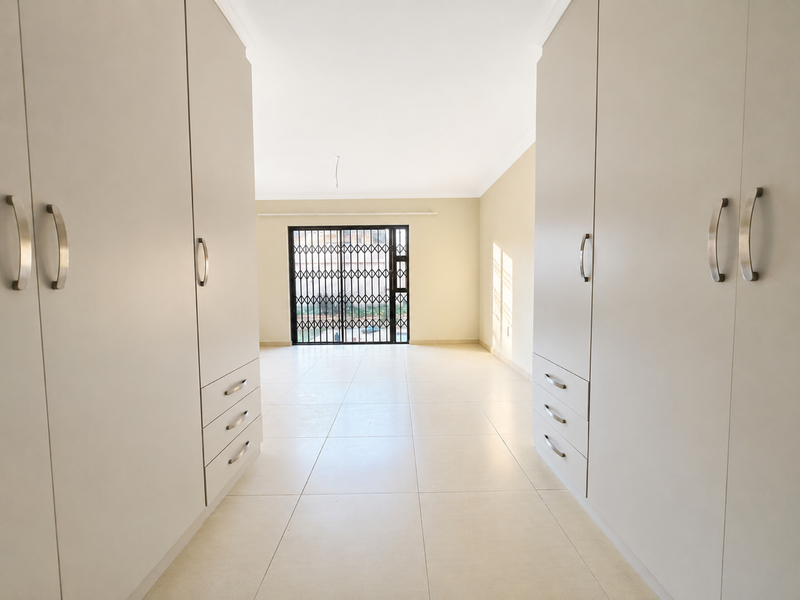Spacious bedroom featuring extensive built-in cupboards, neutral tiled flooring, and a secure sliding door leading to the exterior.