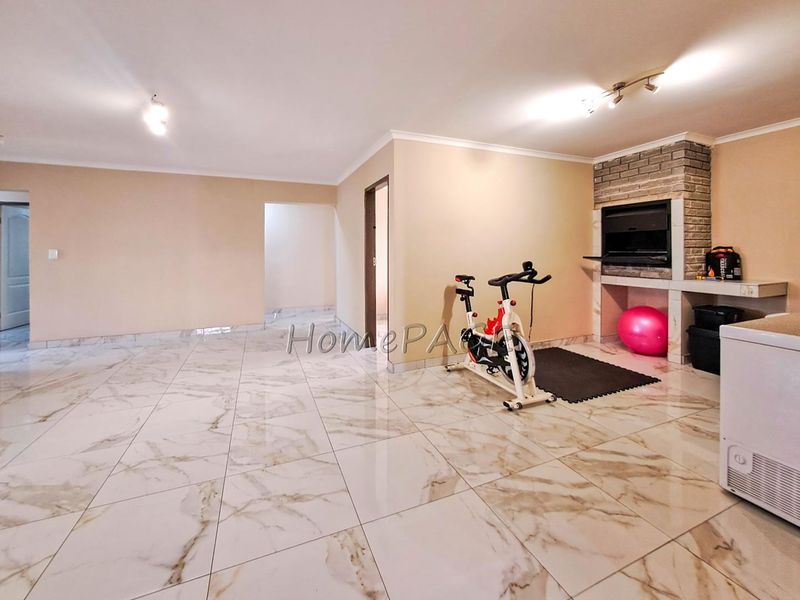Spacious living area featuring polished marble-look floor tiles and a built-in brick fireplace, offering a versatile open-plan layout.