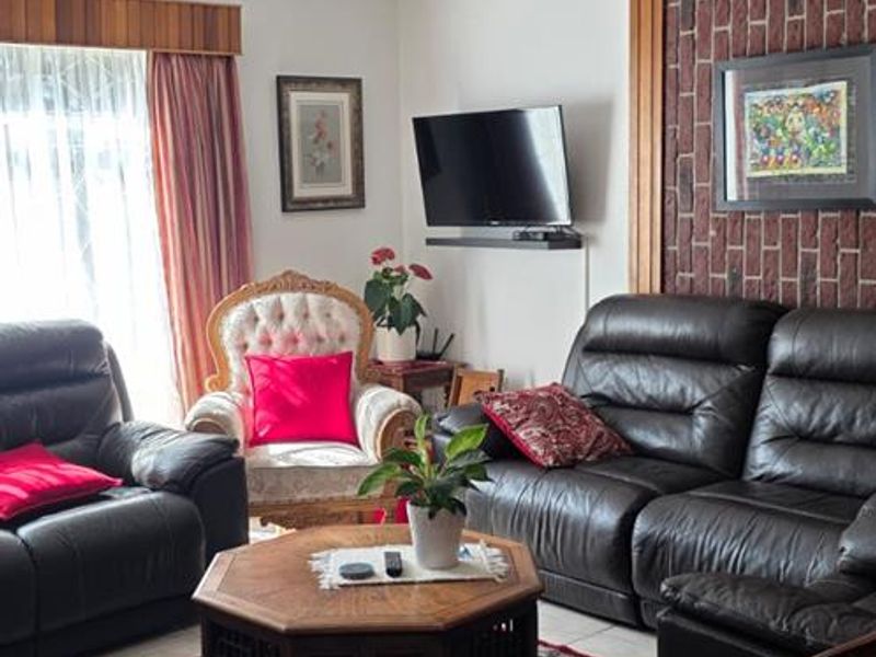 A living room featuring exposed timber ceiling beams, a brick feature wall, and tiled flooring, offering a traditional aesthetic with potential for modern updates.