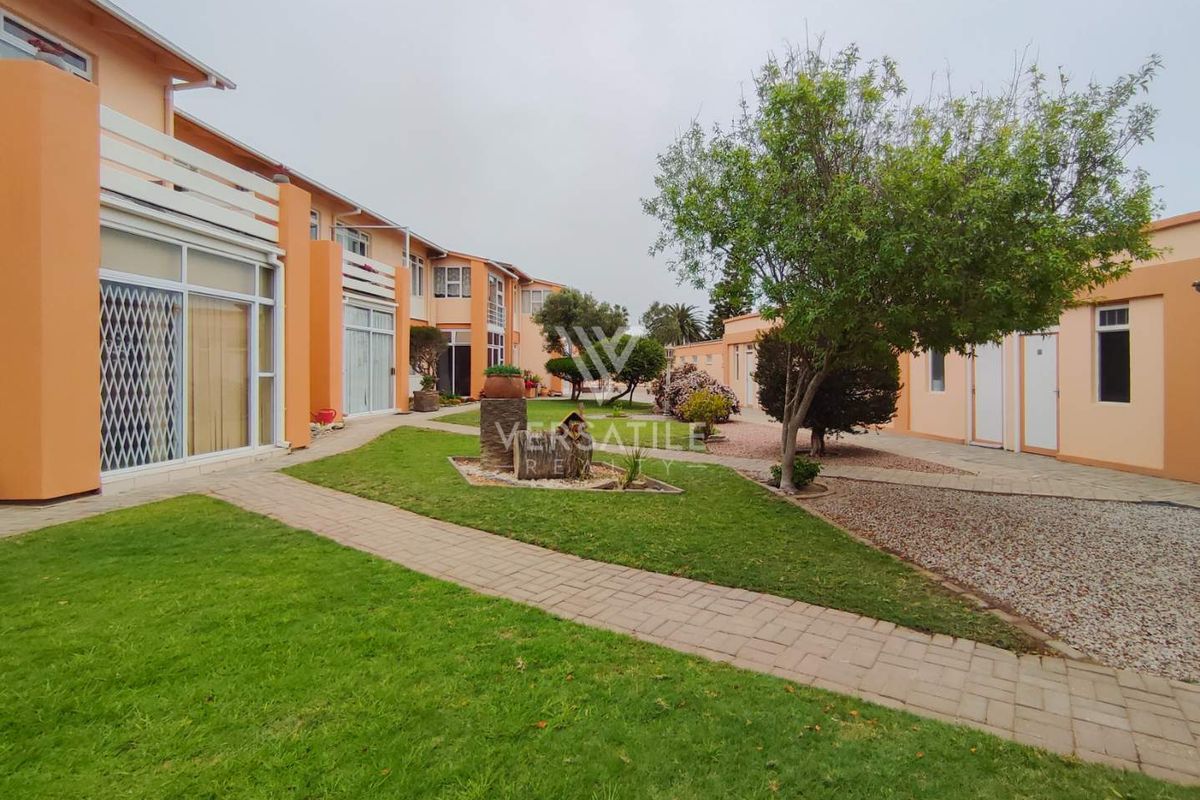 A well-maintained communal garden area featuring paved walkways and access to residential units with sliding glass doors and security gates.