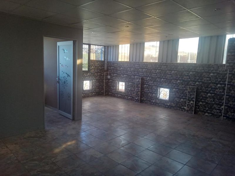 An empty, open-plan living area featuring tiled flooring, a drop ceiling, and decorative brick-effect wall cladding with integrated security gates.