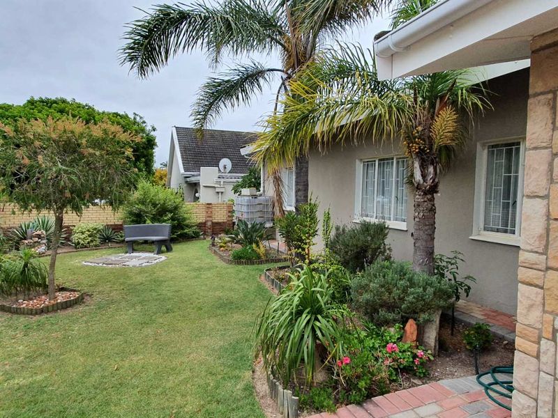 A well-maintained rear garden featuring a lawn, established landscaping, stone-clad exterior wall, and a paved walkway along the side of the house.