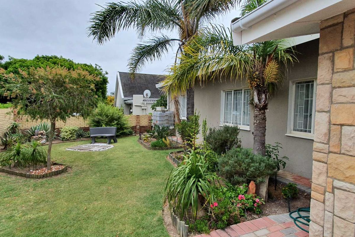 A well-maintained rear garden featuring a lawn, established landscaping, stone-clad exterior wall, and a paved walkway along the side of the house.