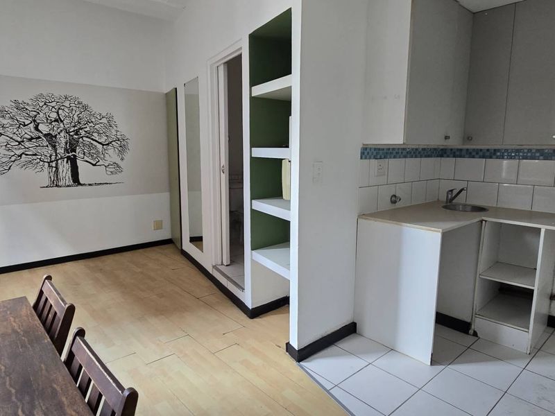 Open-plan living area featuring a compact kitchen with built-in cabinetry, tiled backsplash, and integrated oven, adjacent to a dining space with laminate flooring.