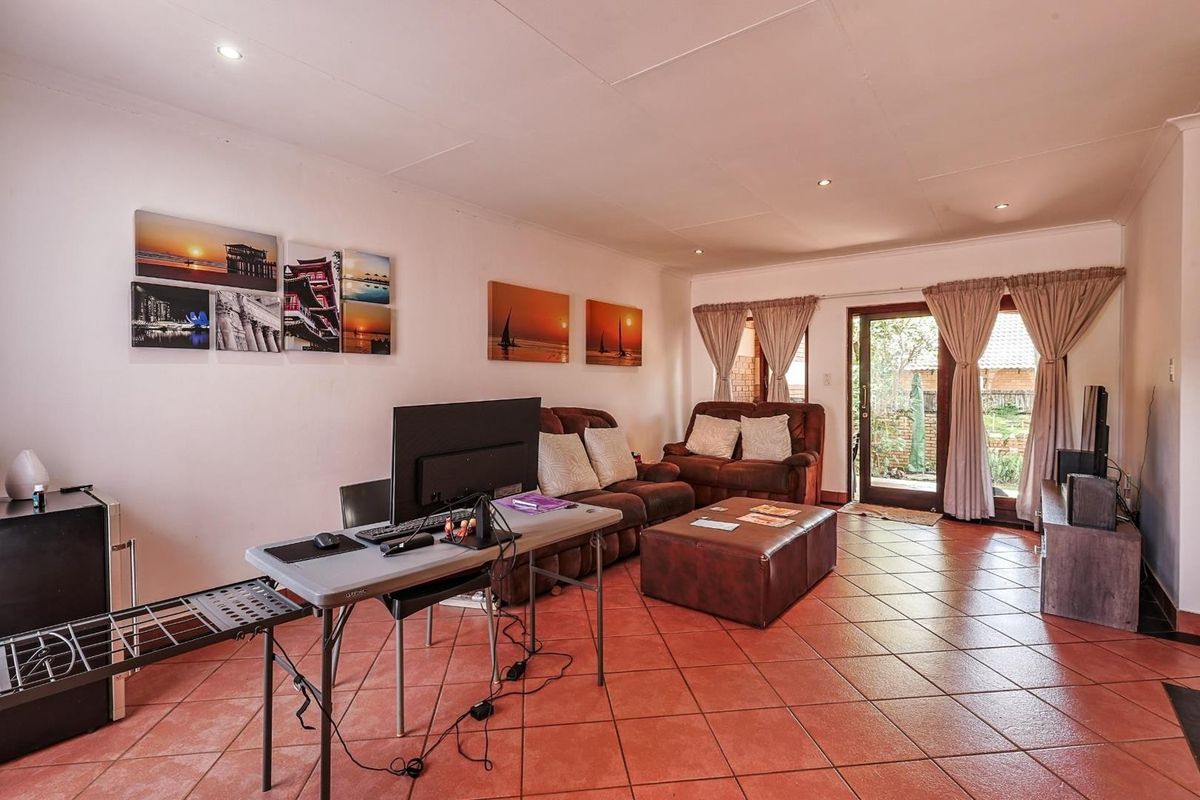 A spacious living room featuring terracotta floor tiles, recessed ceiling lighting, and a glass door providing direct access to the rear garden area.