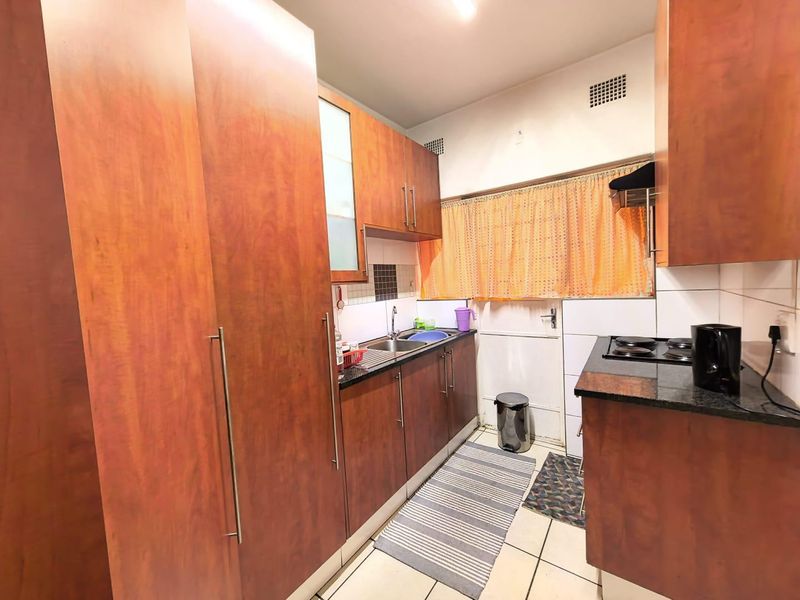 A functional kitchen featuring wood-finish cabinetry, dark countertops, a built-in electric hob, and tiled flooring with a practical layout.