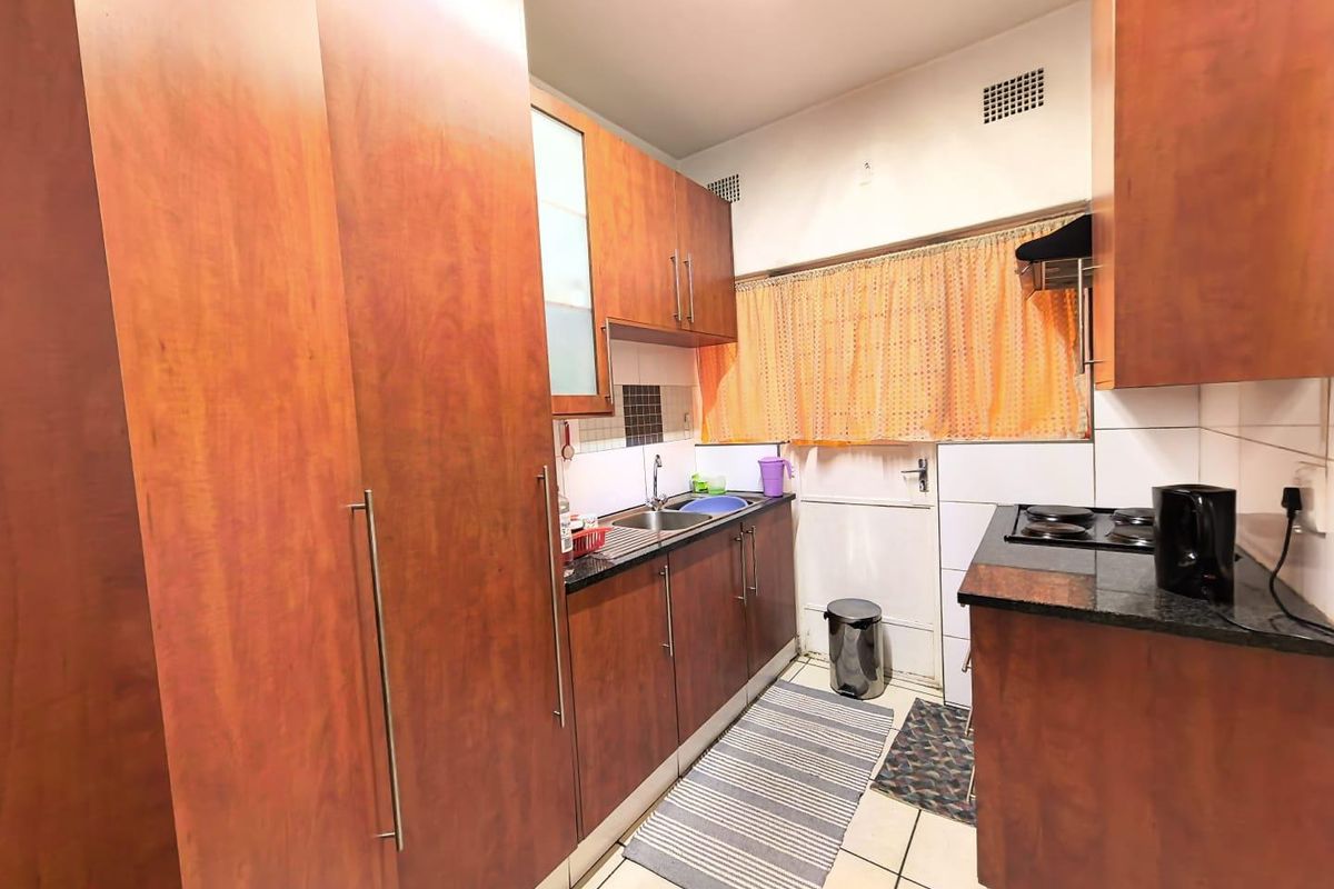 A functional kitchen featuring wood-finish cabinetry, dark countertops, a built-in electric hob, and tiled flooring with a practical layout.
