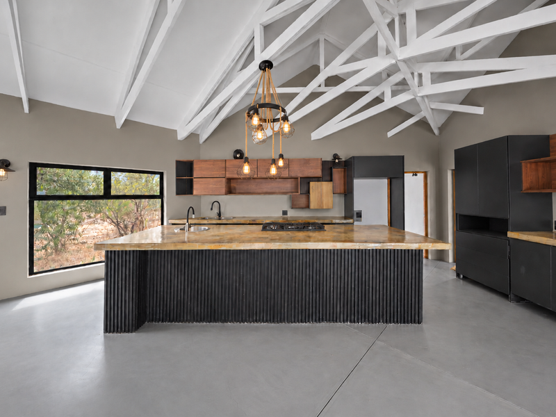 Modern kitchen featuring a large island with a hob, exposed white roof trusses, sleek black cabinetry, and polished concrete floors in an open-plan layout.