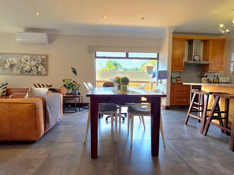 Spacious open-plan living, dining, and kitchen area featuring tiled floors, modern cabinetry, granite countertops, and a split-system air conditioner.