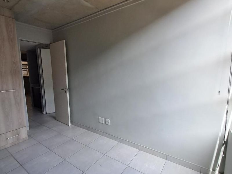 An empty bedroom featuring modern tiled flooring, an exposed concrete ceiling, and a built-in wardrobe with a neutral color palette.