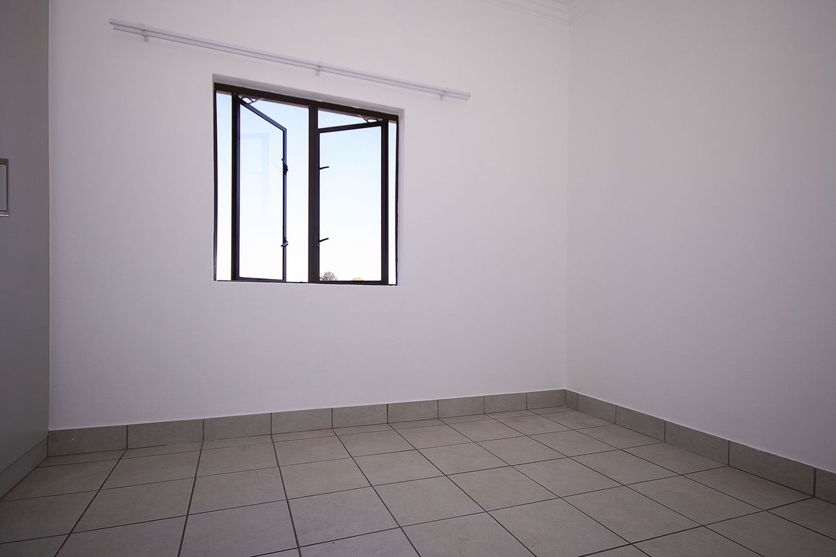 A clean, empty bedroom featuring neutral tiled flooring, white walls, and a functional casement window with an installed curtain rod.