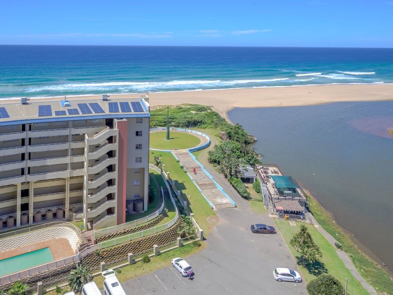Aerial view of an apartment complex featuring solar panels, a swimming pool, and direct access to the beach and river estuary.