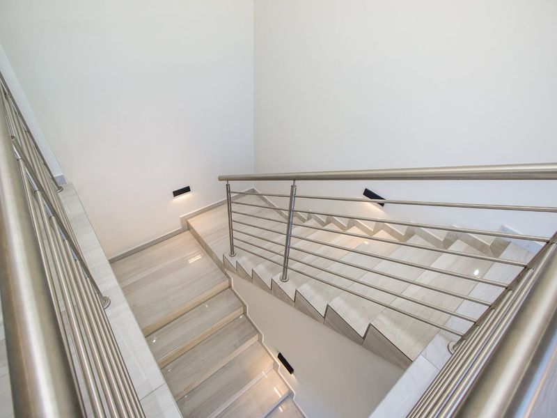 Modern staircase featuring tiled steps, sleek stainless steel railings, and integrated recessed wall lighting for a clean, contemporary aesthetic.