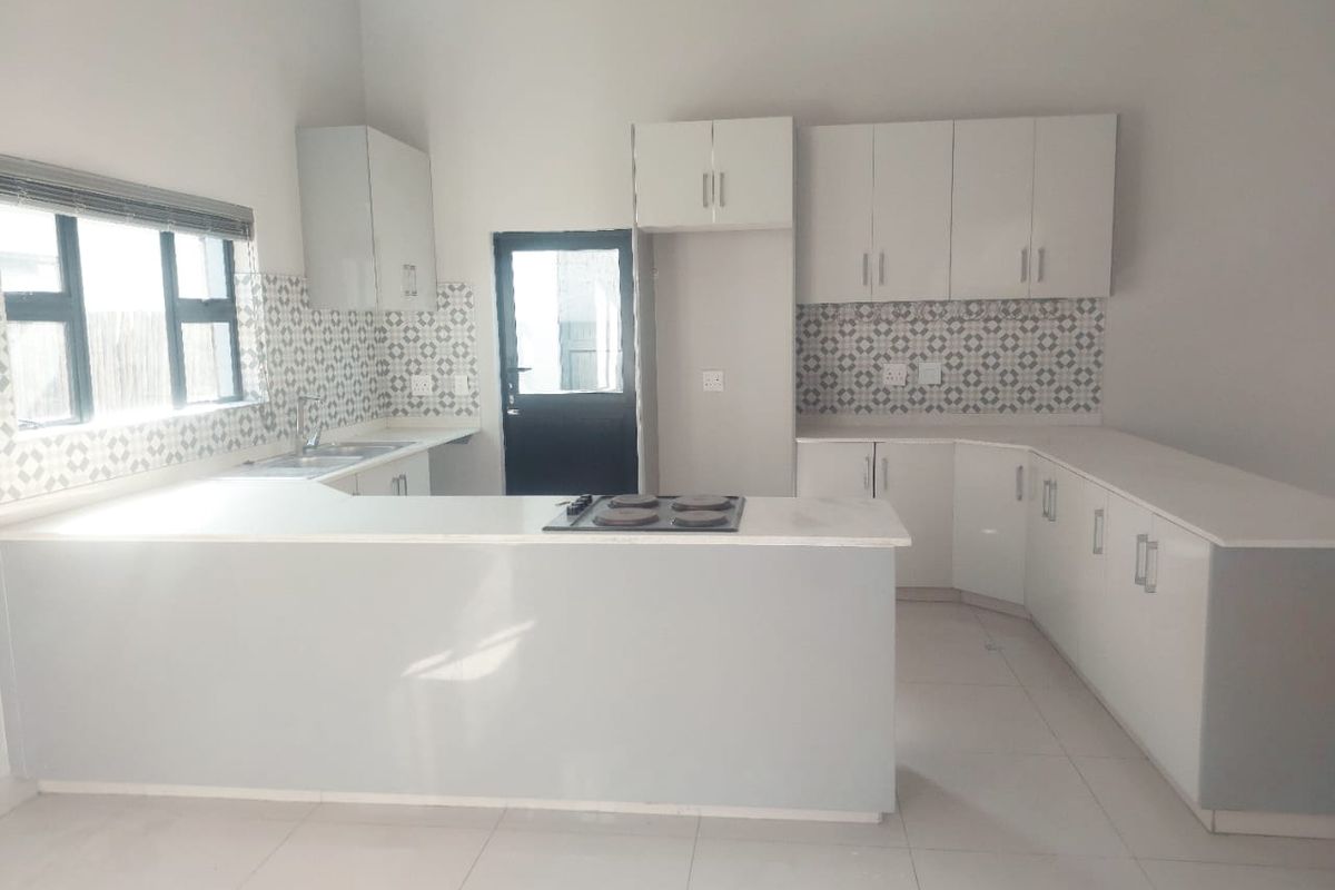 Modern kitchen featuring white built-in cabinetry, stone countertops, a tiled backsplash, and an integrated electric hob with direct access to the exterior.