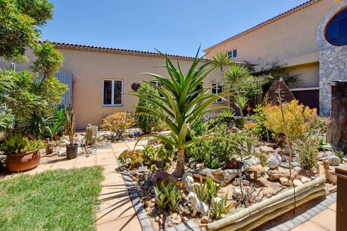 A well-maintained rear courtyard featuring a landscaped garden, tiled pathways, and stone-clad architectural details under a clear blue sky.