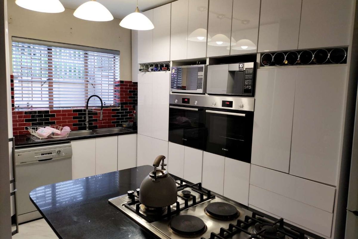 Modern kitchen featuring high-gloss white cabinetry, black granite countertops, a central island with a gas hob, and integrated double ovens.