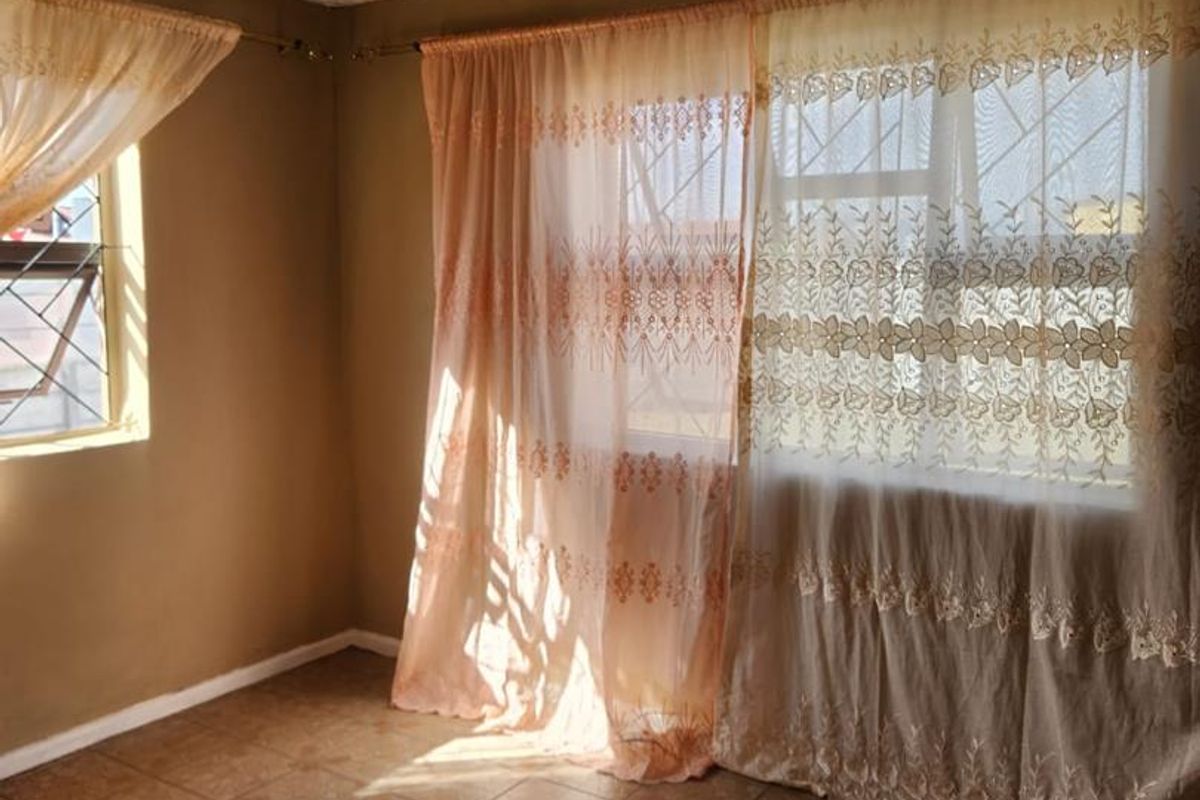 An empty living room featuring tiled flooring, security bars on the windows, and a ceiling light fixture, ready for a fresh update.