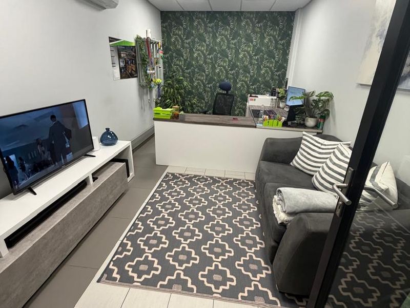 A functional office space featuring tiled flooring, a built-in desk, air conditioning, and a suspended ceiling with recessed lighting.